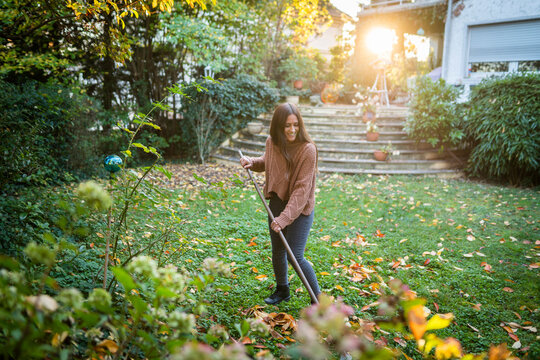 "Lady maintaining a clean lawn by raking colorful fall leaves during autumn garden care."