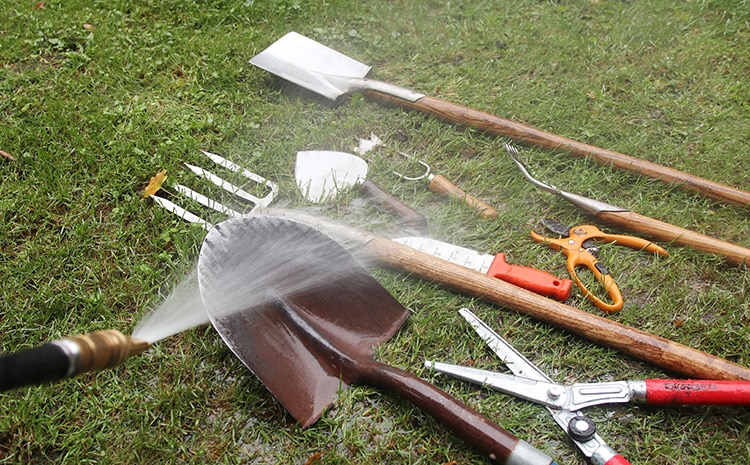 "Cleaning gardening tools with a hose to remove dirt and debris before storing them."